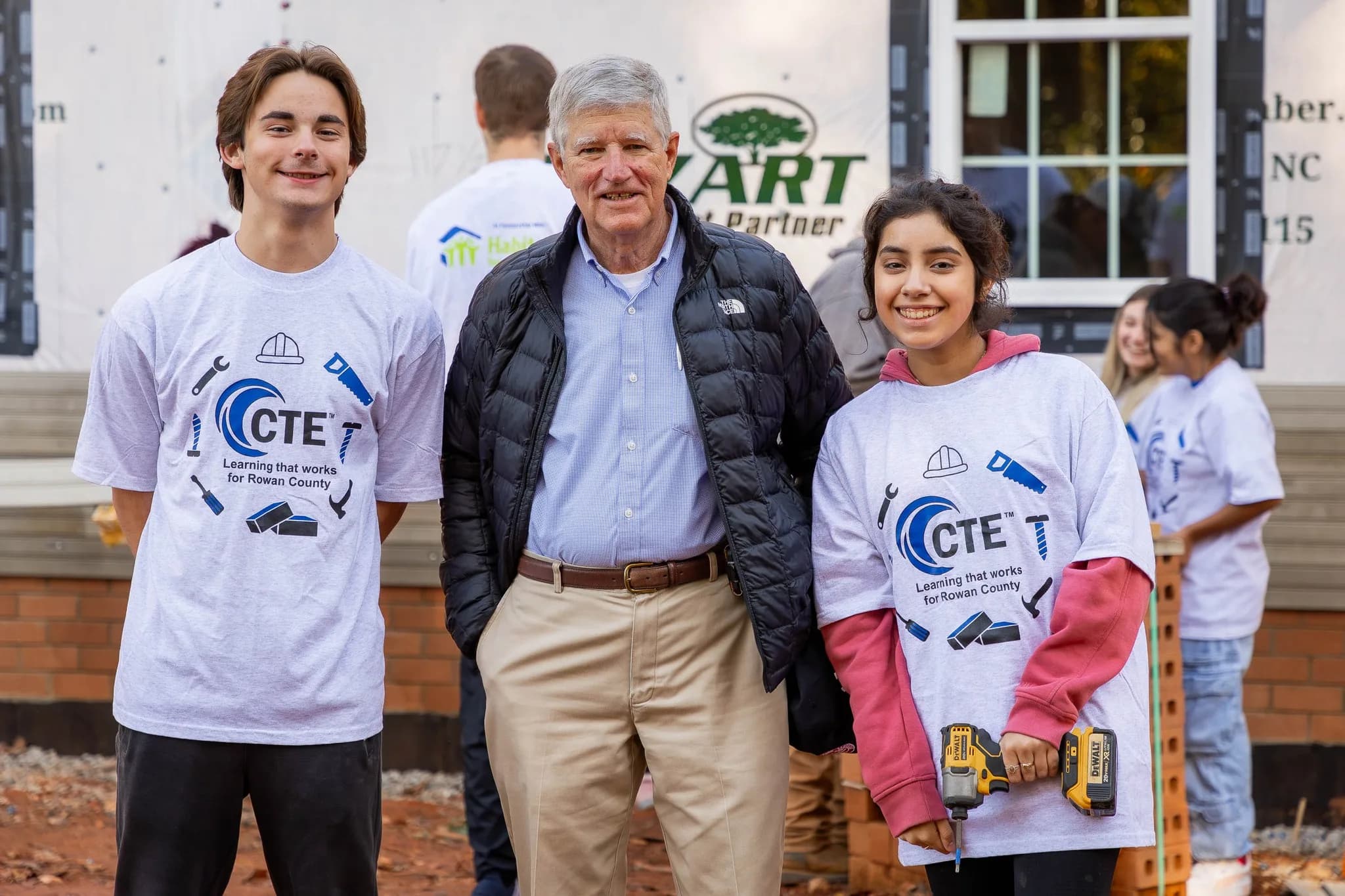 Volunteers in matching shirts smiling in front of a house under construction